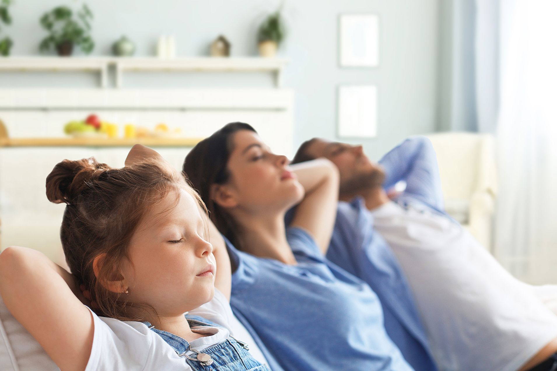 A family is sitting on a couch with their hands behind their heads.
