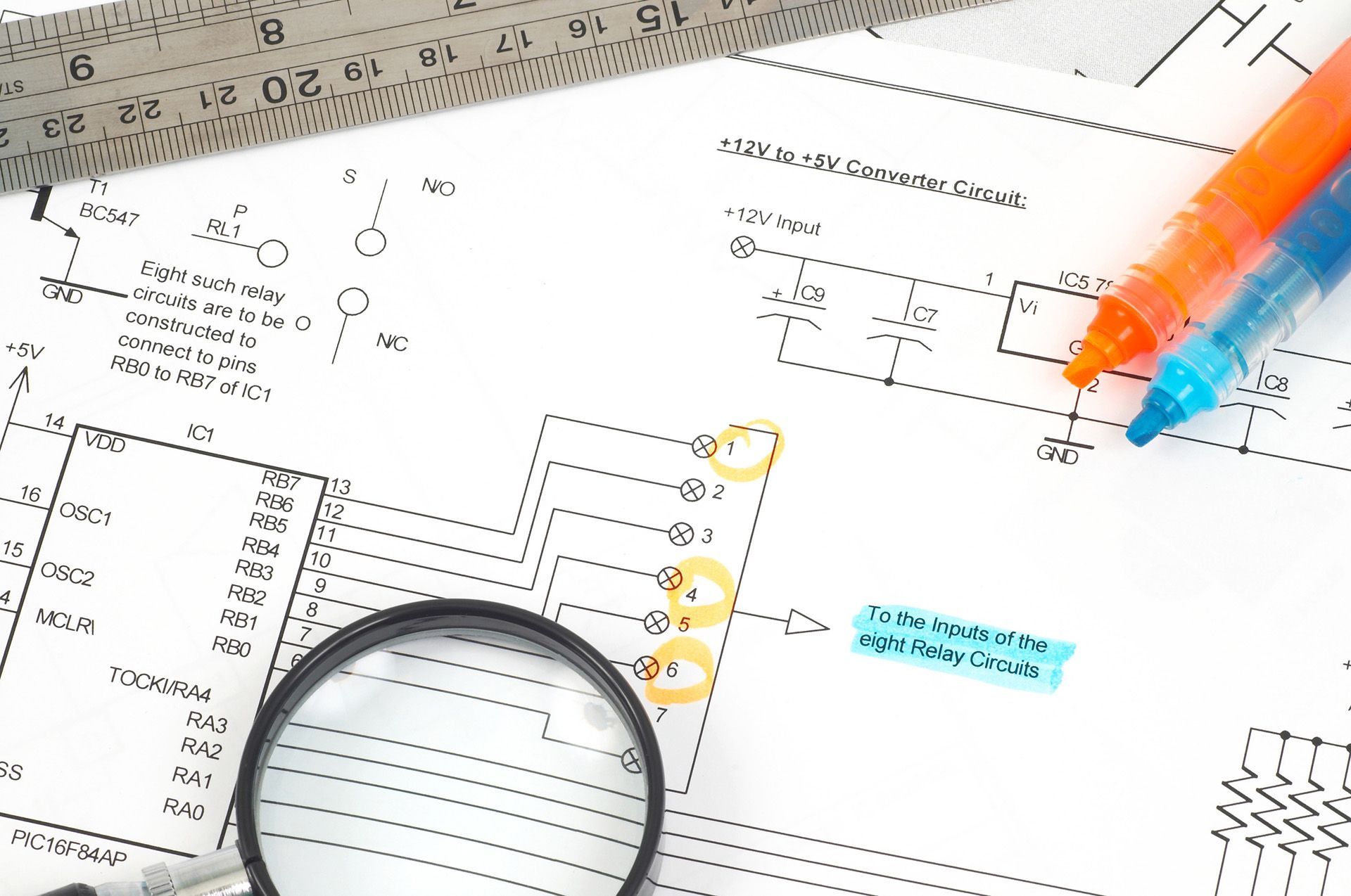 A magnifying glass sits on top of a piece of paper containing electrical plans.