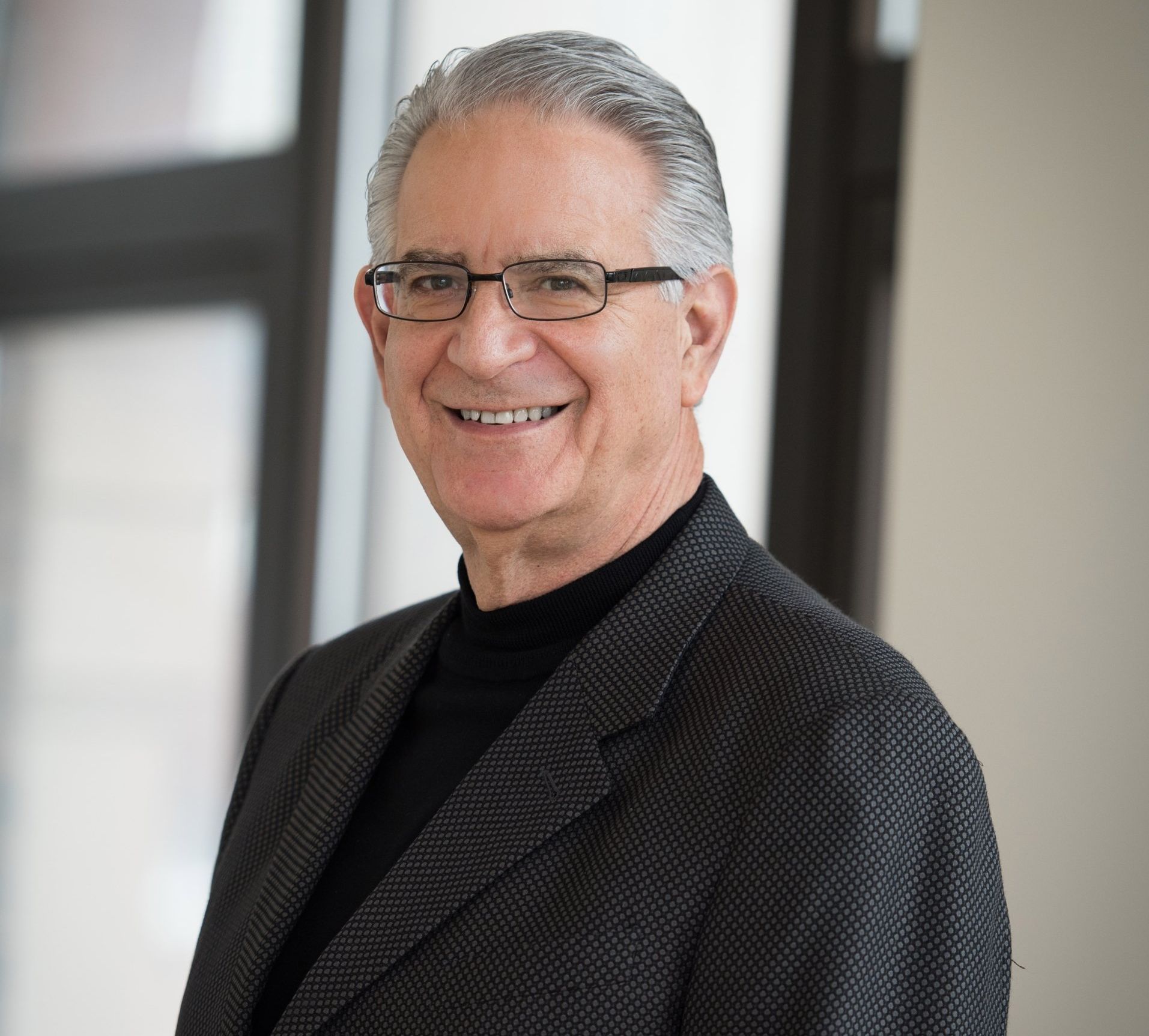 A man wearing glasses and a suit is smiling for the camera