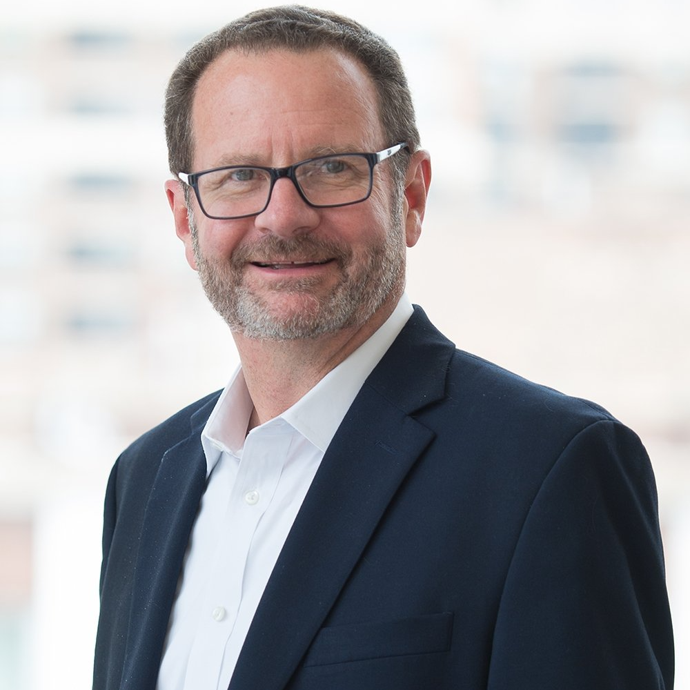 A man wearing glasses and a suit is smiling for the camera