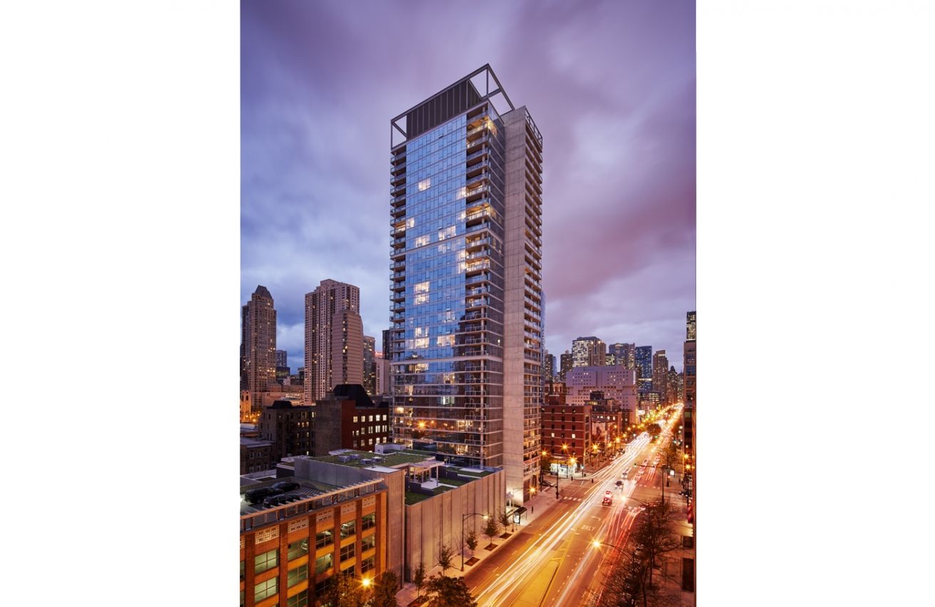 A tall building with a lot of windows is in the middle of a city at night.