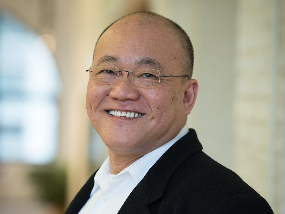 A bald man wearing glasses and a black jacket is smiling for the camera.