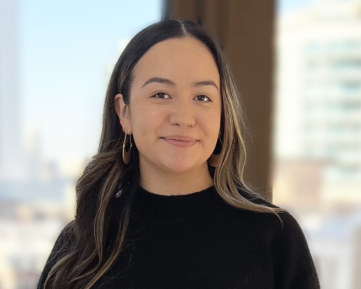 A woman in a black sweater is standing in front of a window.