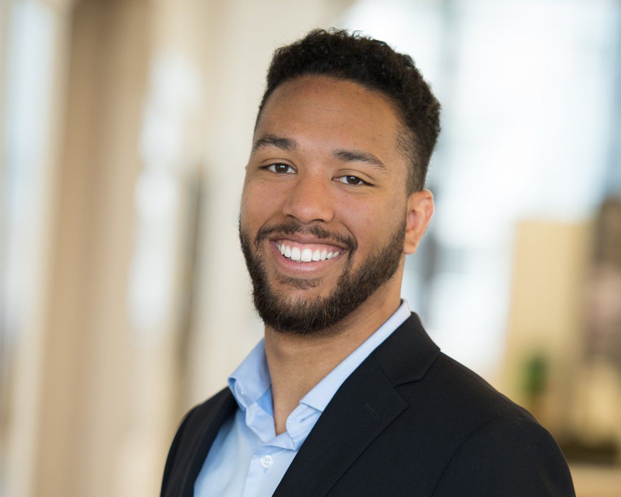 A man with a beard is wearing a suit and smiling for the camera.