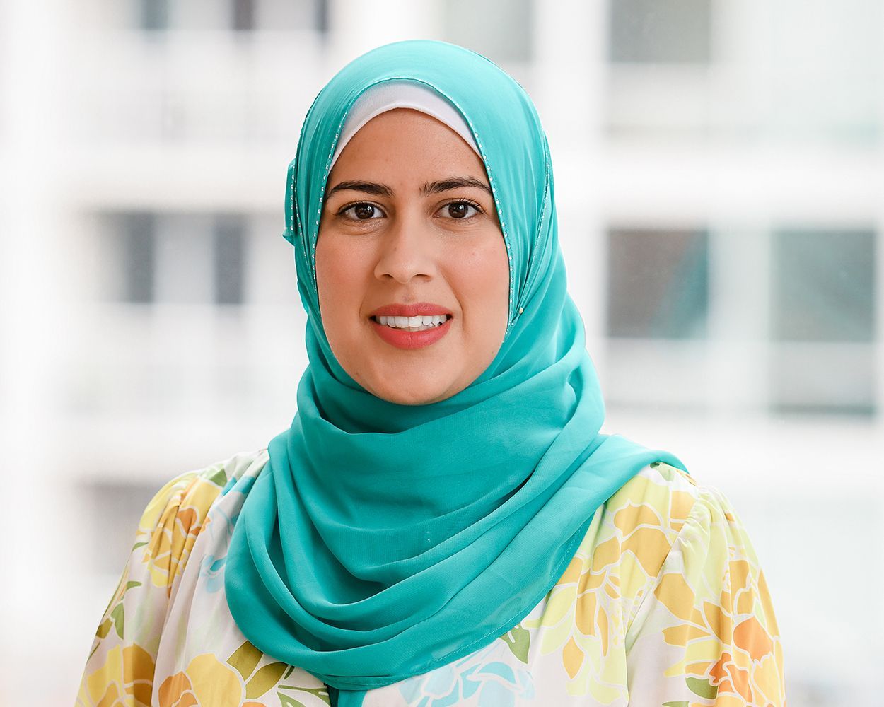 A woman wearing a blue hijab is smiling for the camera.