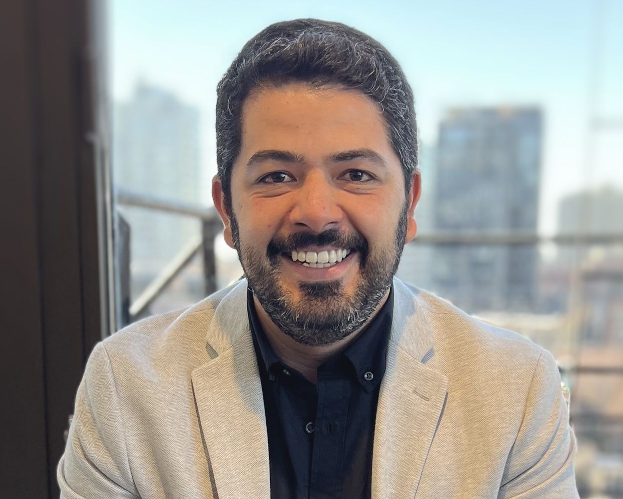 A man with a beard is smiling for the camera in front of a window.