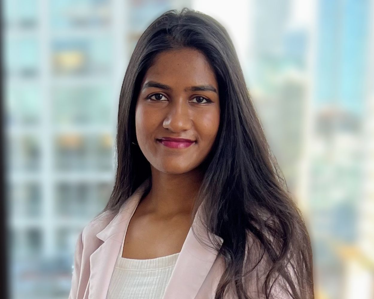 A woman in a pink jacket is standing in front of a window.