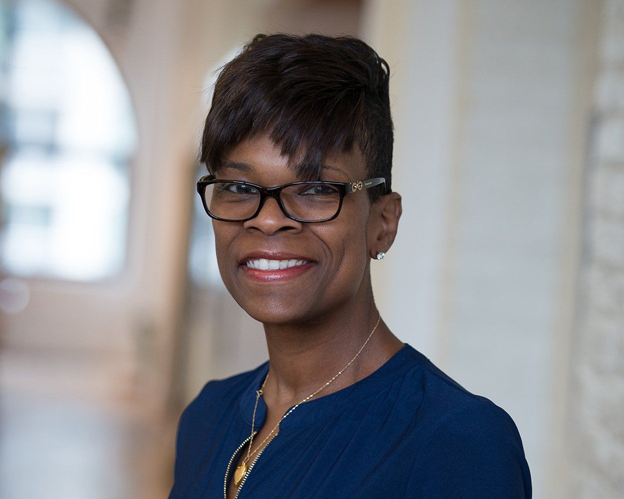 A woman wearing glasses and a blue shirt is smiling for the camera.