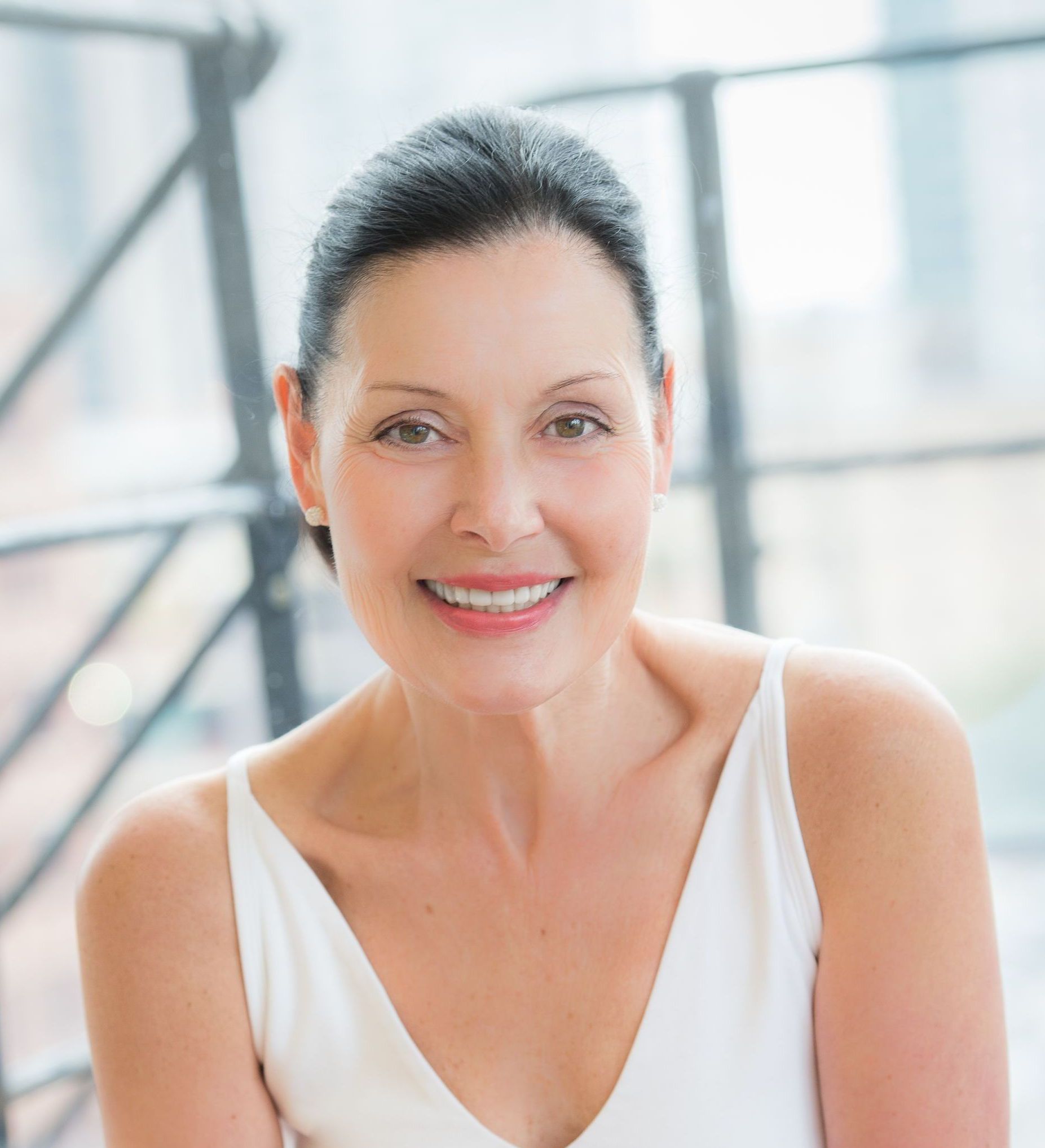 A woman in a white tank top is smiling for the camera.
