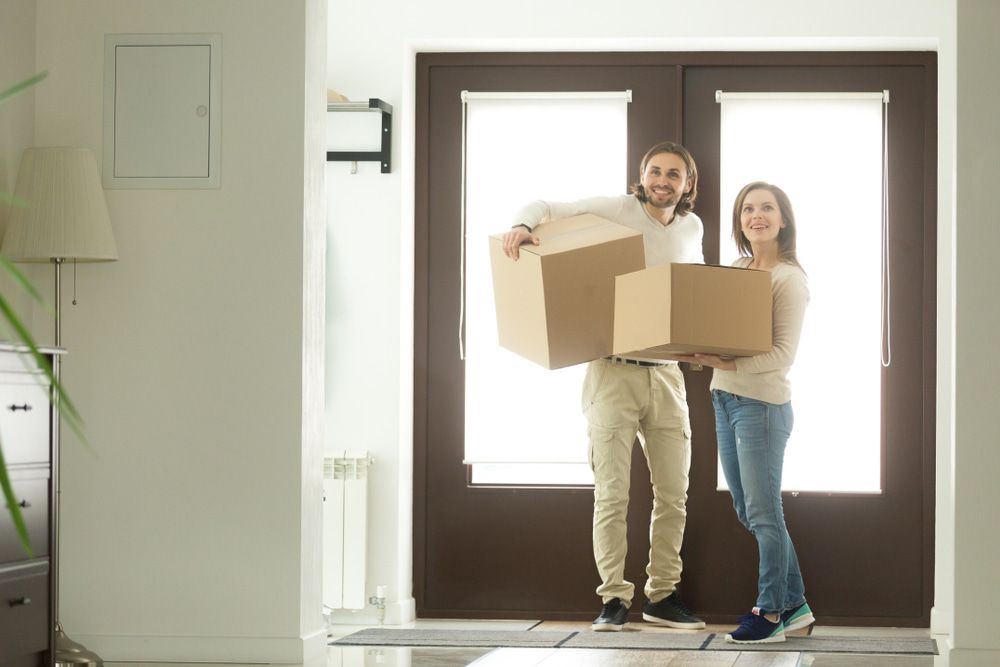 A Man And A Woman Are Carrying Cardboard Boxes Into A New Home — Removalists In Ballina