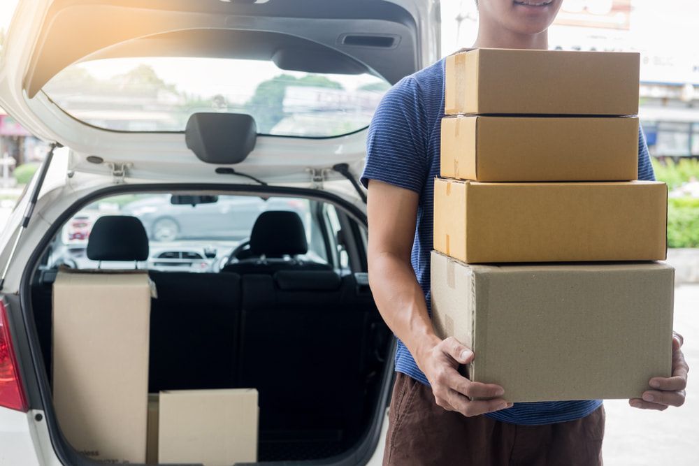 A Man Is Holding A Stack Of Cardboard Boxes In Front Of A Car — Professional Removalists In Alstonville