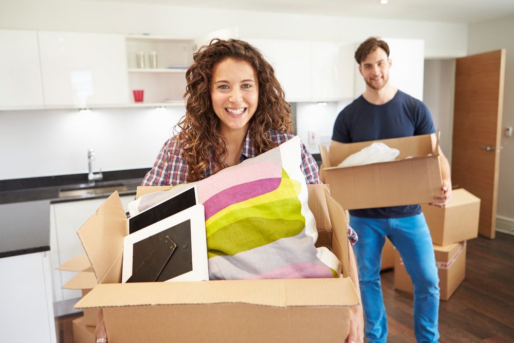 A Man And A Woman Are Holding Cardboard Boxes In A Kitchen — Removalist In Alstonville