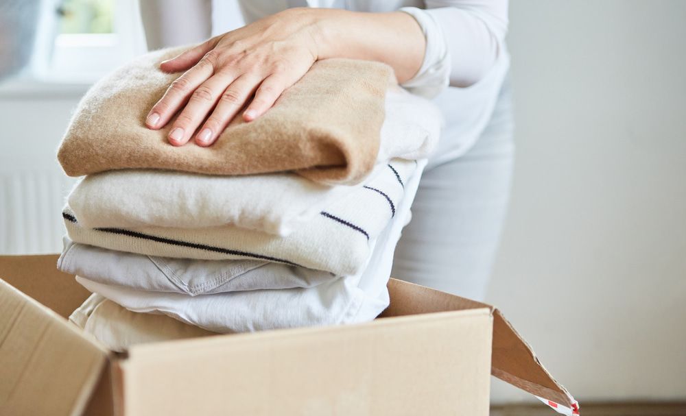 A Person Is Putting Clothes In A Cardboard Box — Removalist In Alstonville