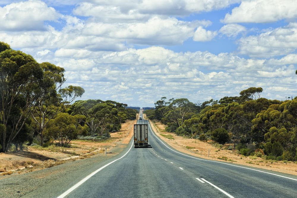 A Truck Is Driving Down An Empty Highway Surrounded By Trees — Removalist In Yamba