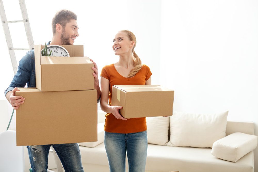 A Man And A Woman Are Carrying Cardboard Boxes In A Living Room — Removalists In Tweed Heads