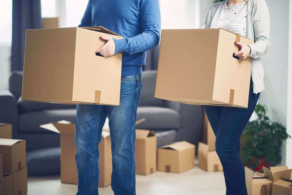 A Man And A Woman Are Holding Cardboard Boxes In A Living Room — Removalists In Byron Bay