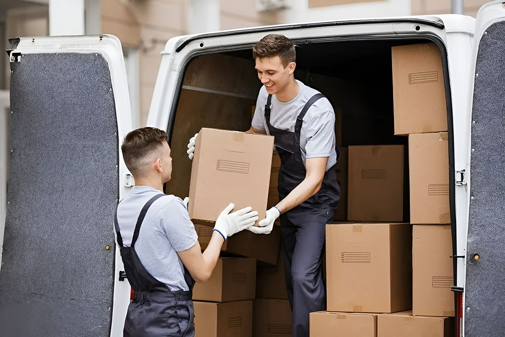 Two Men in Overalls Loading Cardboard Boxes into a White Van