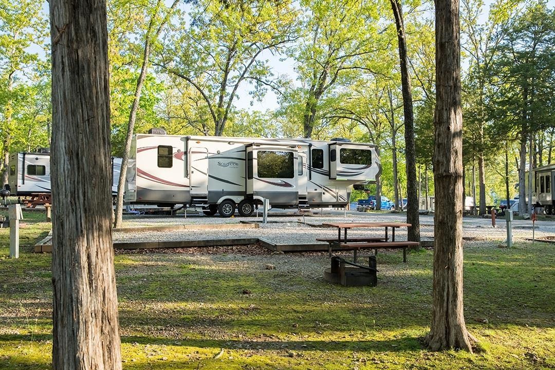 A rv is parked in a campground surrounded by trees.