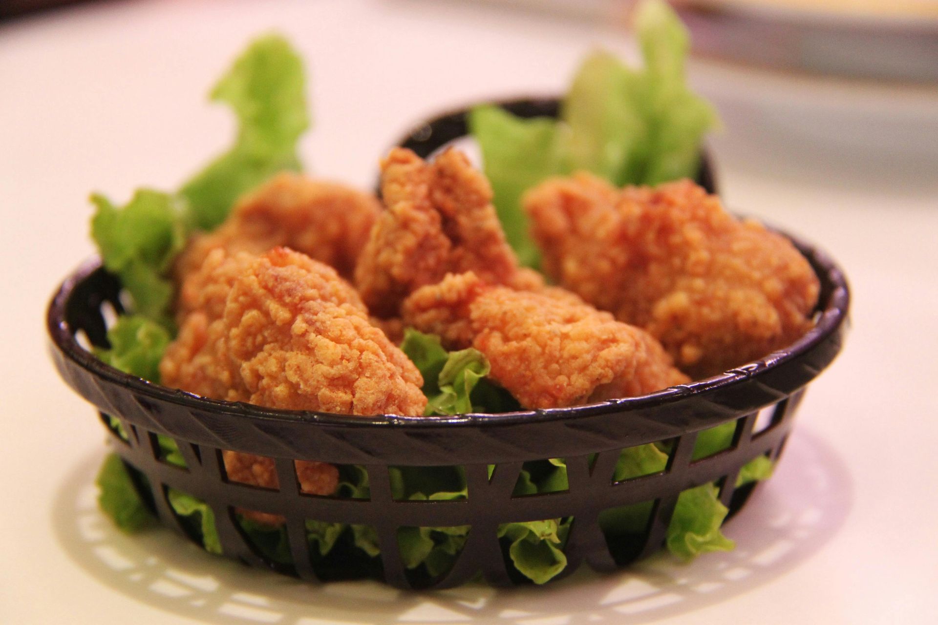 A basket filled with fried chicken and lettuce on a table.