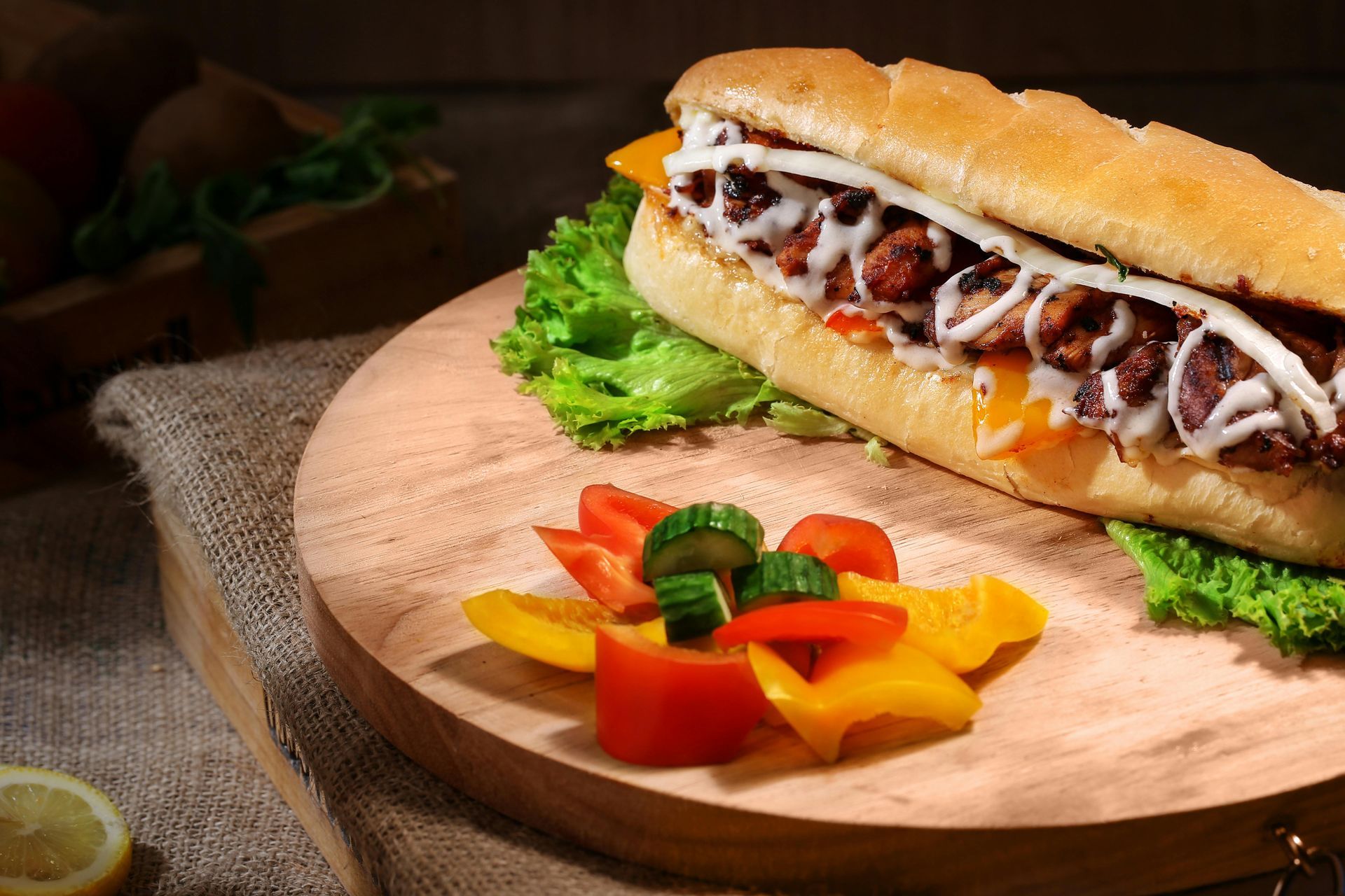 A sub sandwich is sitting on a wooden cutting board with vegetables.
