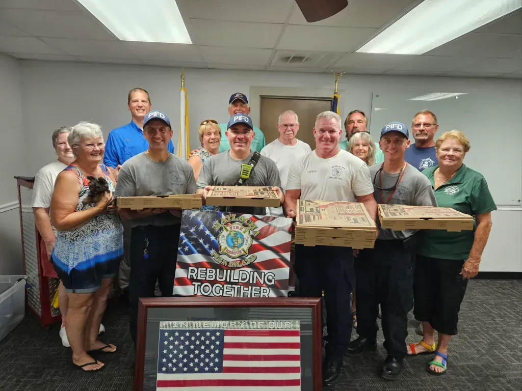 A group of people are standing in a room holding pizza boxes.