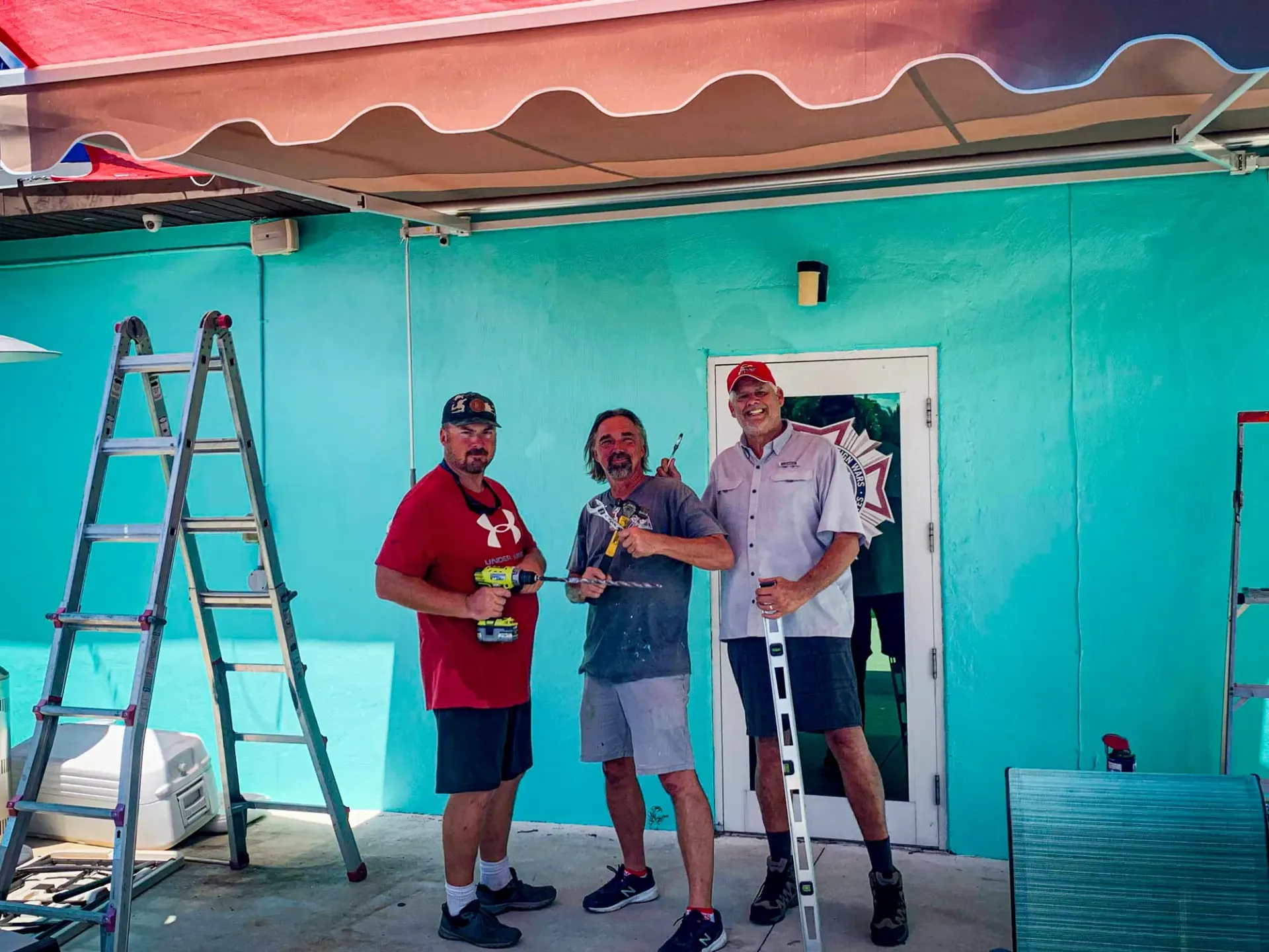 Three men are standing in front of a blue building.