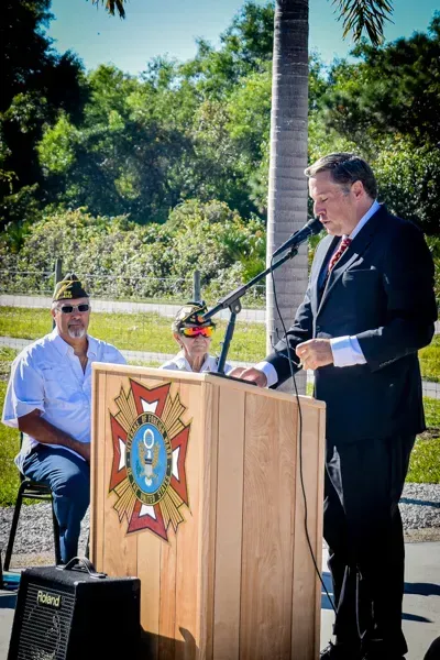 A man in a suit and tie is standing at a podium talking into a microphone.