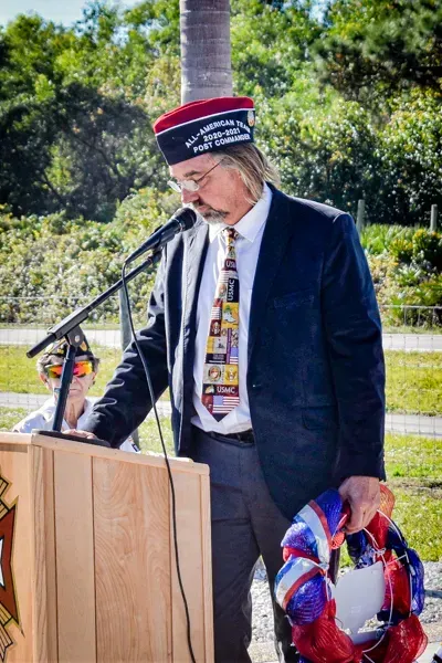 A man in a suit and tie is standing at a podium holding a wreath.
