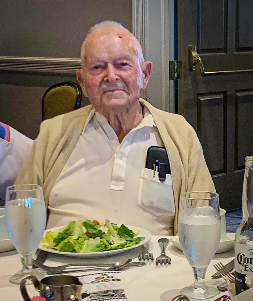 A man is sitting at a table with a plate of food and glasses of water.