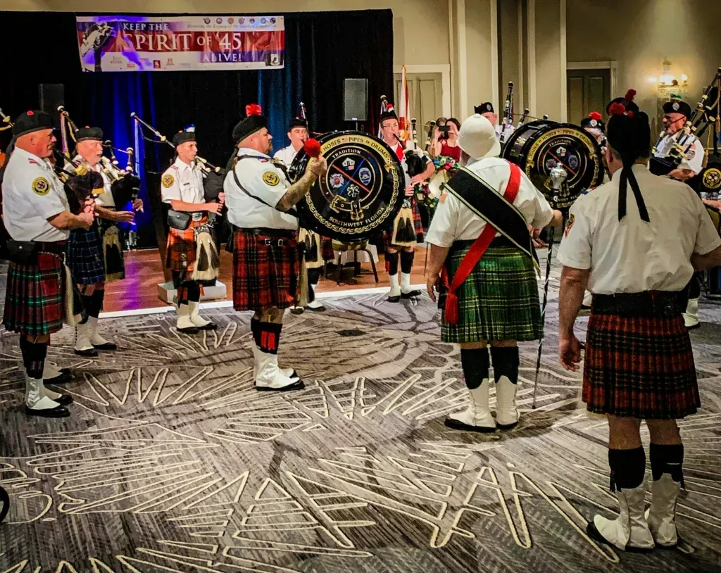 A group of men in kilts are playing bagpipes in a room.