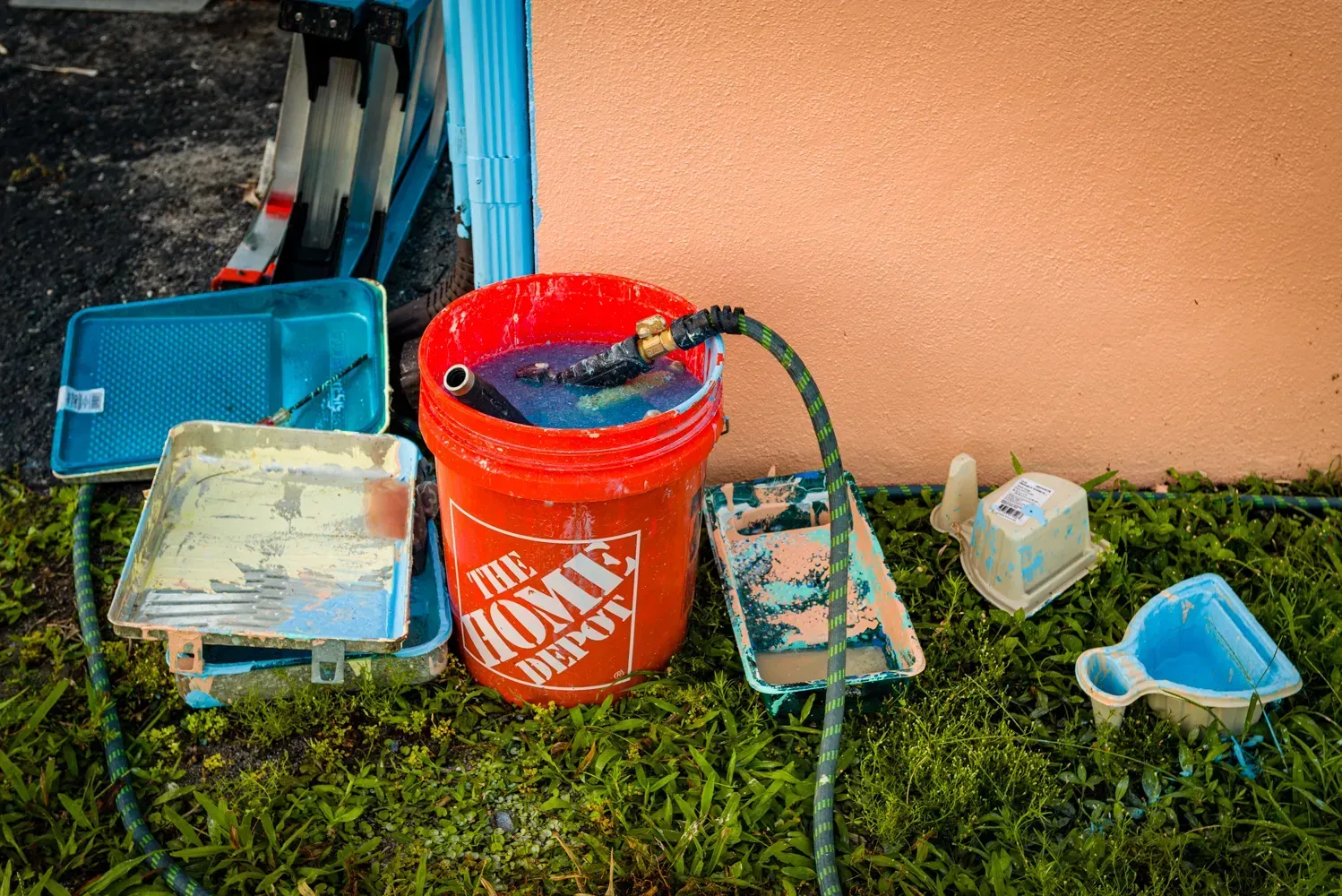 A bucket of paint is sitting on the grass next to a hose.