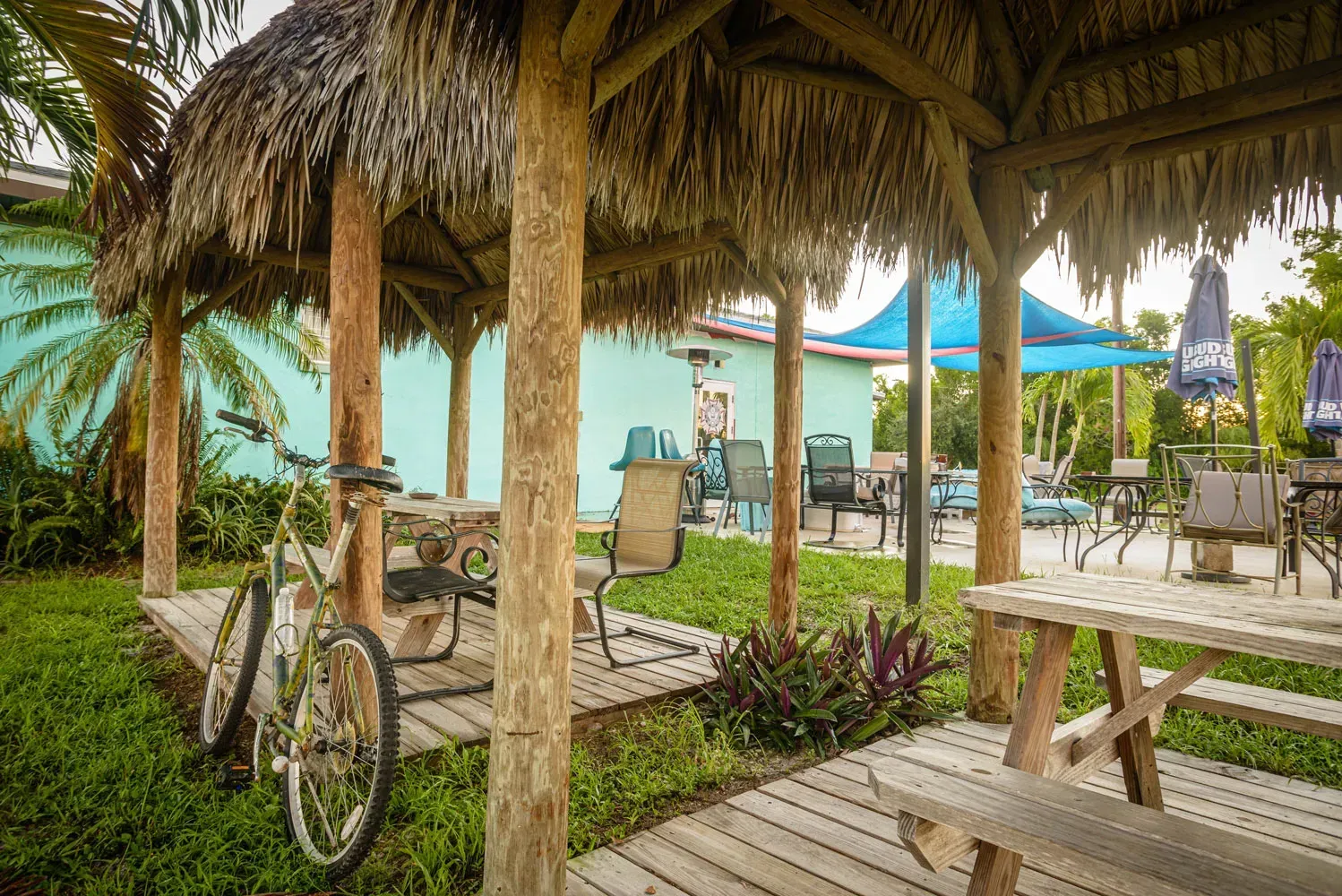 A bicycle is parked under a thatched gazebo next to a picnic table.