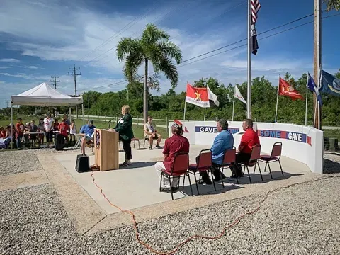 A woman is standing at a podium giving a speech to a group of people sitting in chairs.