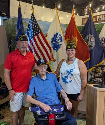 A man in a wheelchair is posing for a picture with two other people in front of flags.