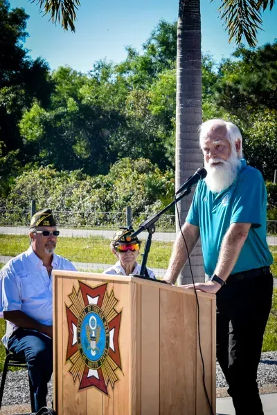A man with a beard is standing at a podium talking into a microphone.
