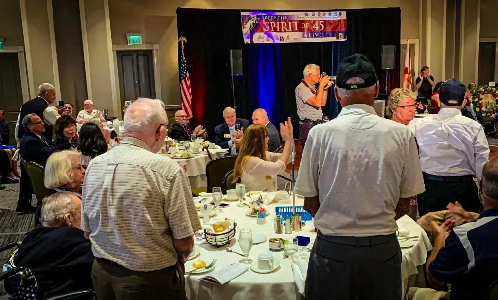 A group of people are sitting at tables in a room watching a man sing on stage.
