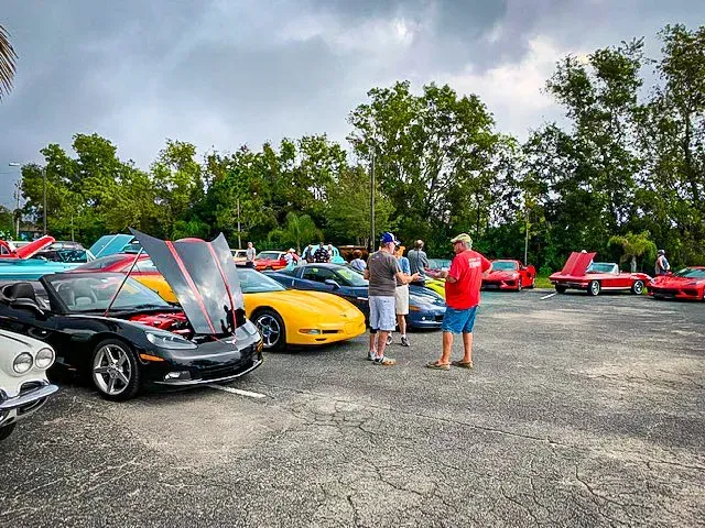 A group of people are standing in a parking lot looking at cars.