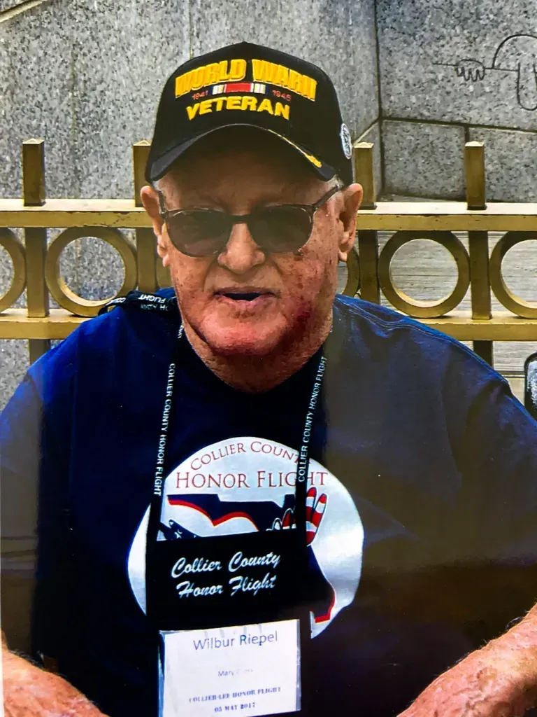 A man wearing a hat and sunglasses is standing in front of a fence.