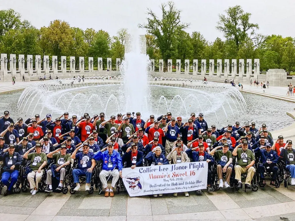 A group of people in wheelchairs salute in front of a fountain