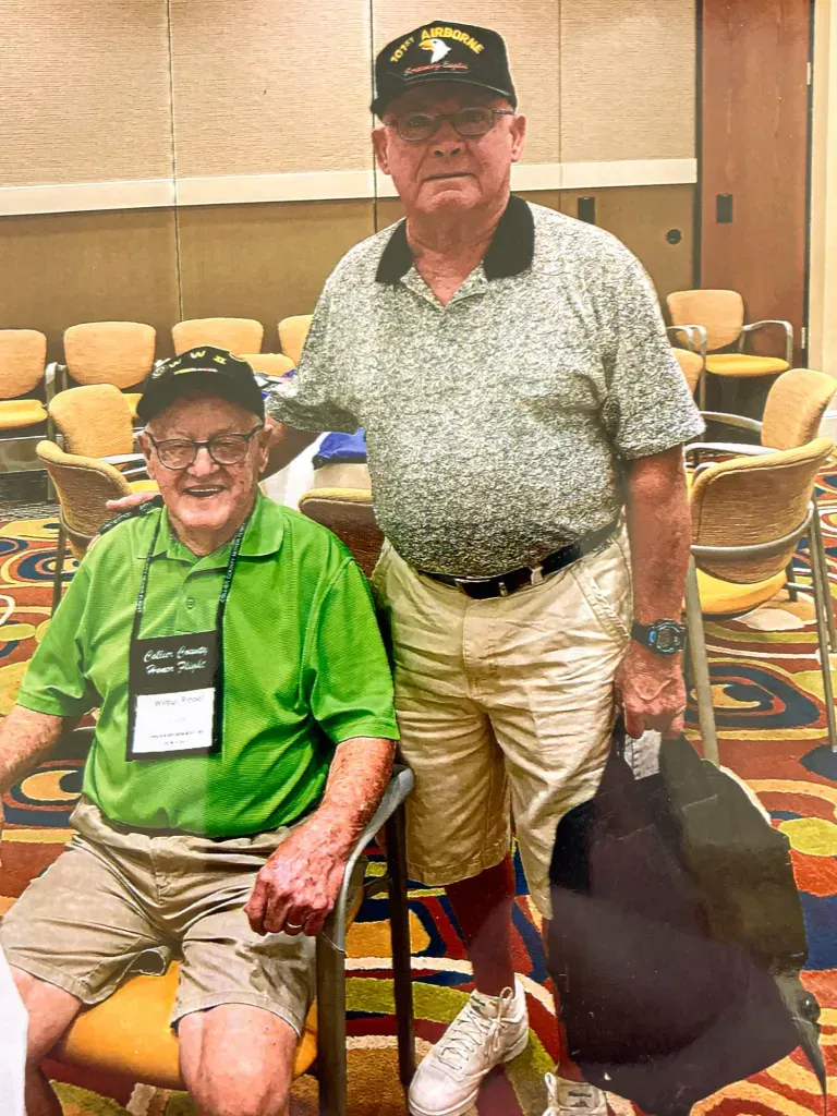 Two men are posing for a picture in a room . one of the men is wearing a green shirt.