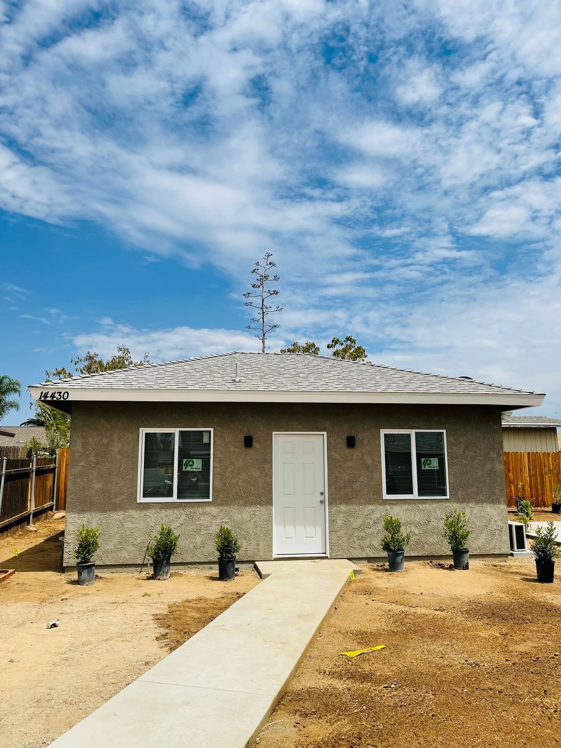 Two-story house with dark roof, white garage door, beige siding, and blue shutters on a cloudy day.