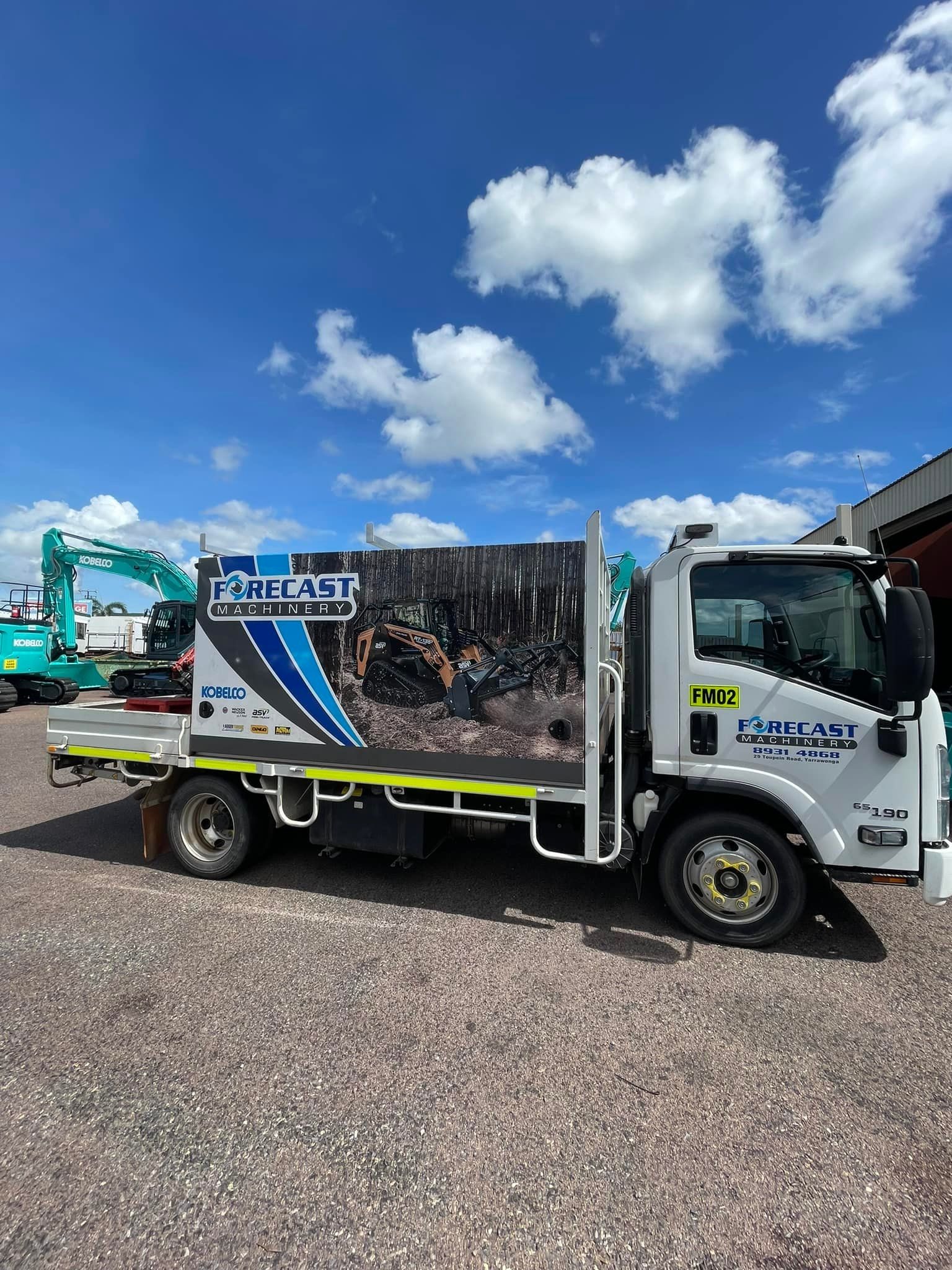A white service truck with branded decals parked on a gravel lot under a blue sky, with construction equipment nearby — Forecast Machinery in Yarrawonga, NT