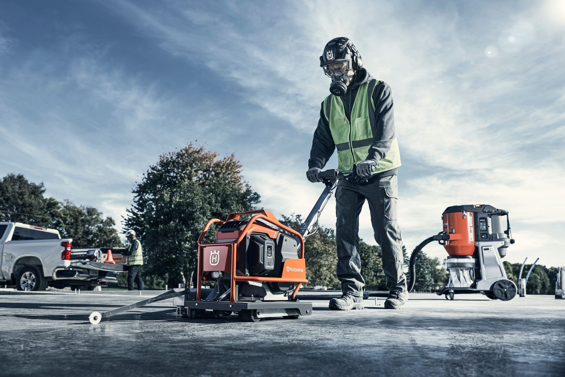 A worker in safety gear operates an orange floor grinder on a construction site with a vacuum unit nearby — Forecast Machinery in Yarrawonga, NT