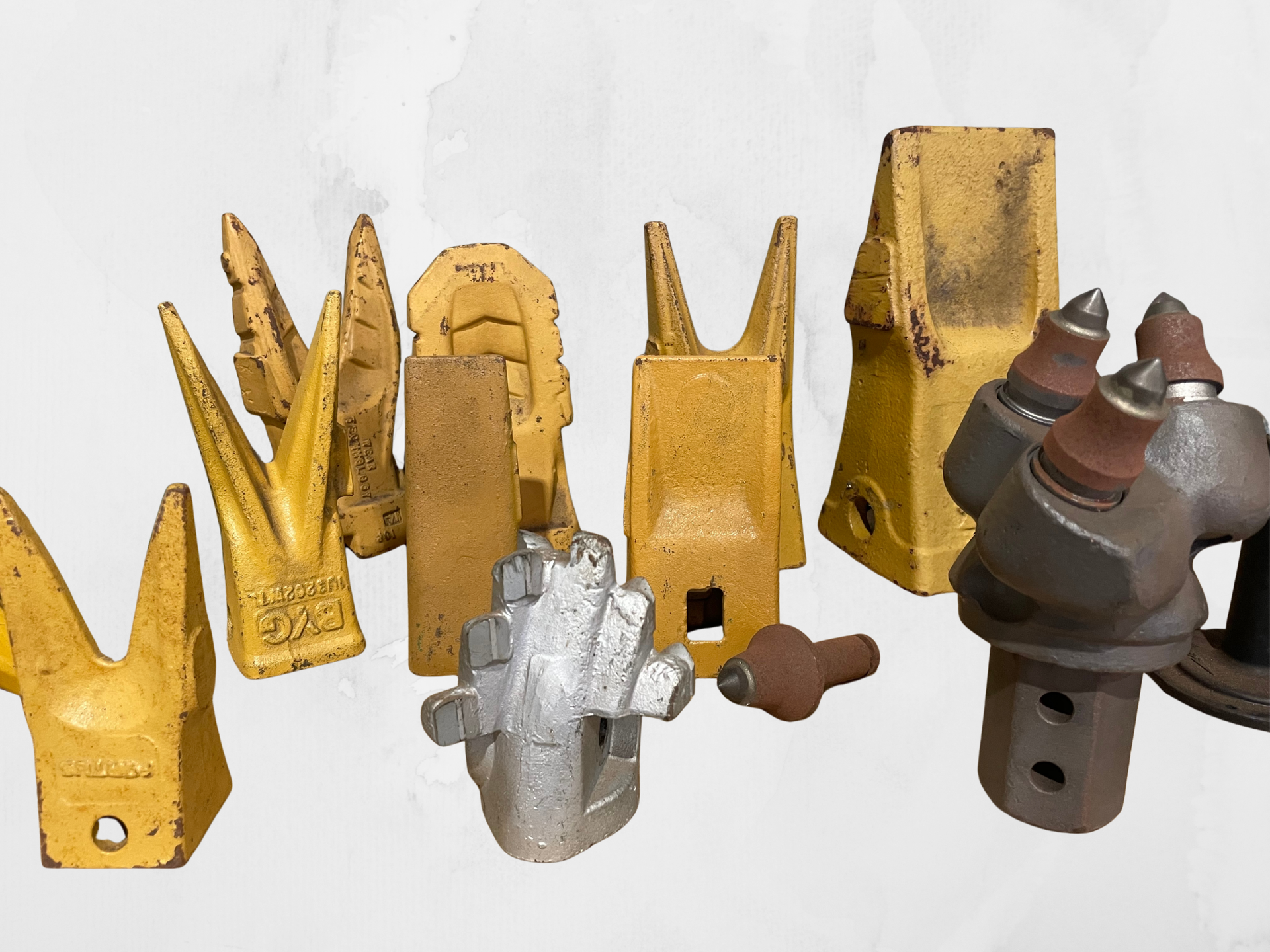 A collection of various yellow and metallic heavy-duty construction equipment teeth and drill bits against a white background — Forecast Machinery in Yarrawonga, NT