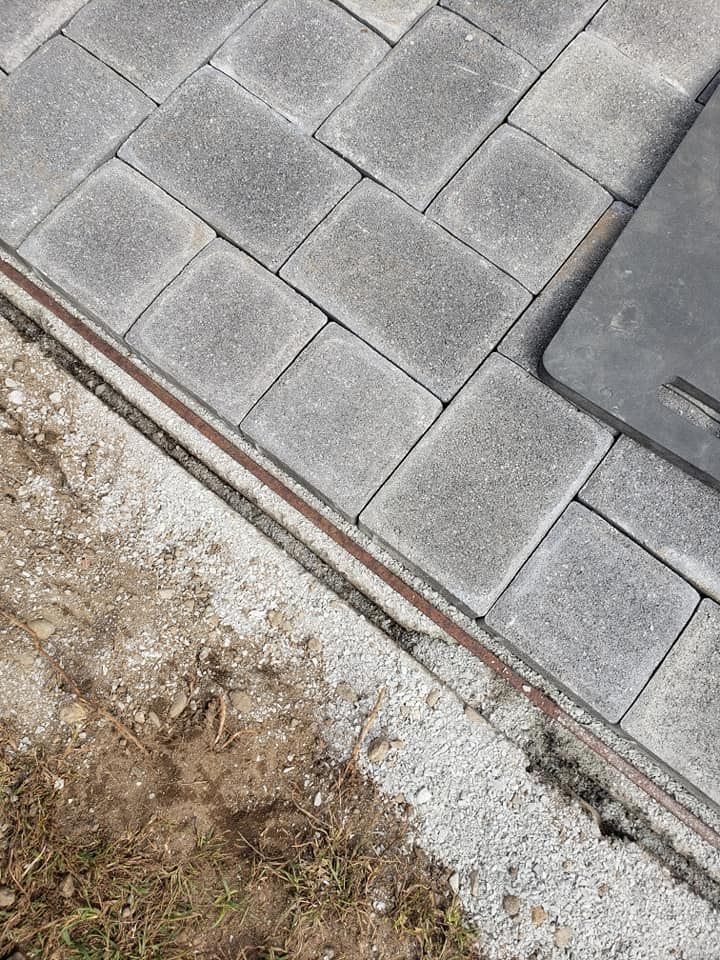 Gray pavers bordering a gravel path and dirt, with a metal edging strip.