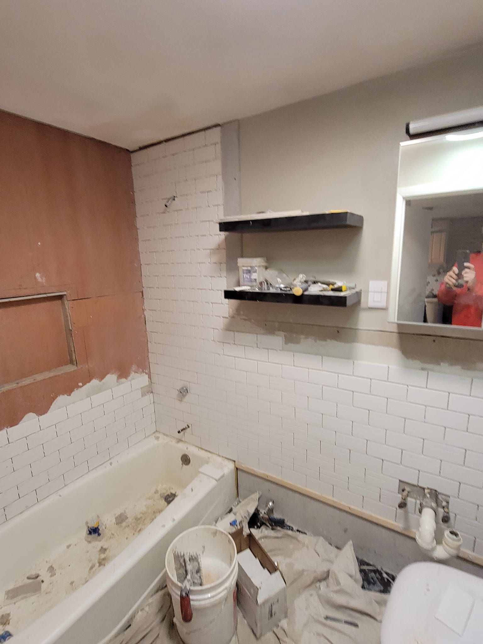 Bathroom renovation in progress; white subway tile on walls, shelves, tub, and sink installed.