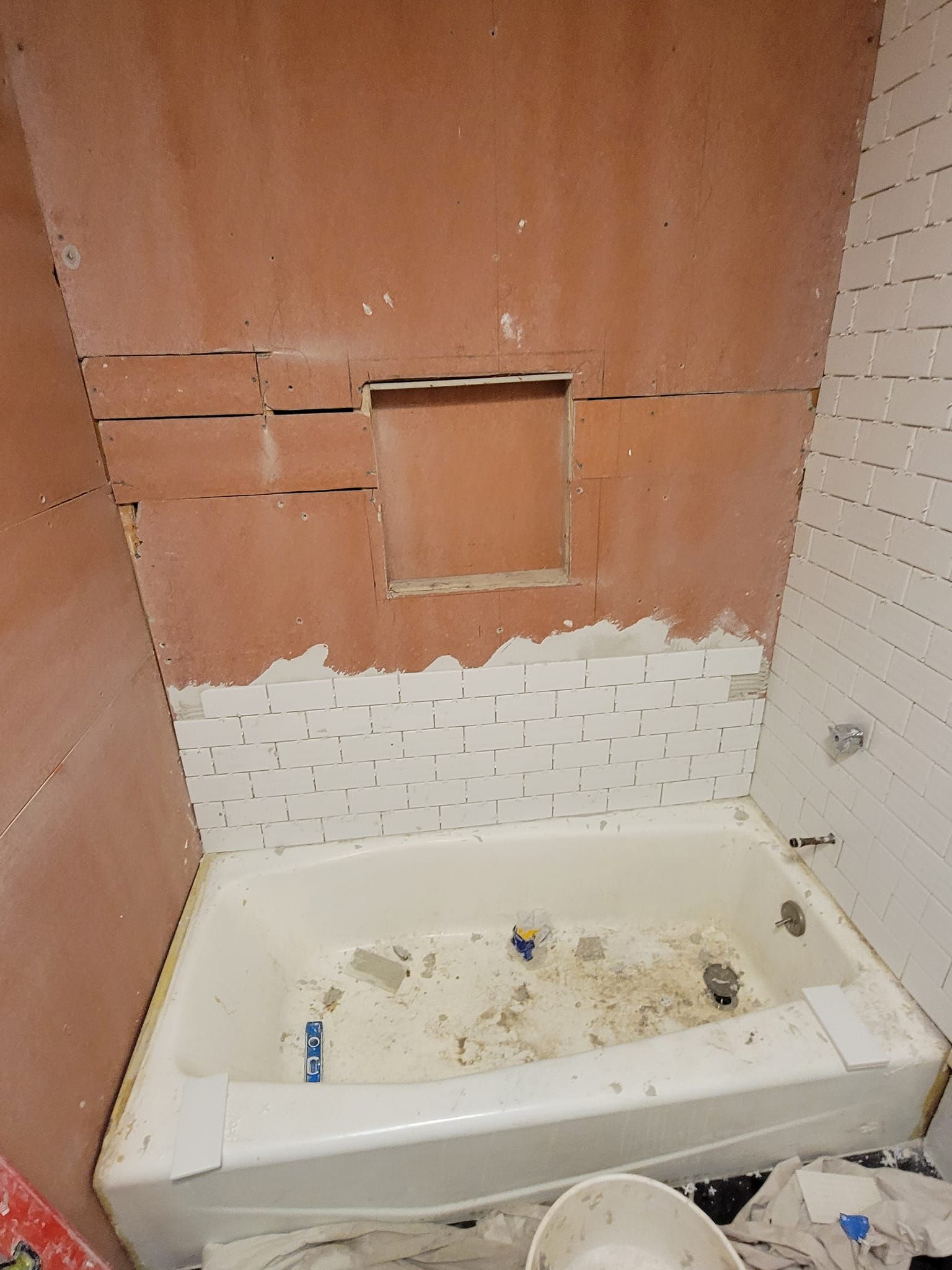 Bathroom renovation in progress; tub with partially tiled wall and built-in niche. Drywall and mortar visible.