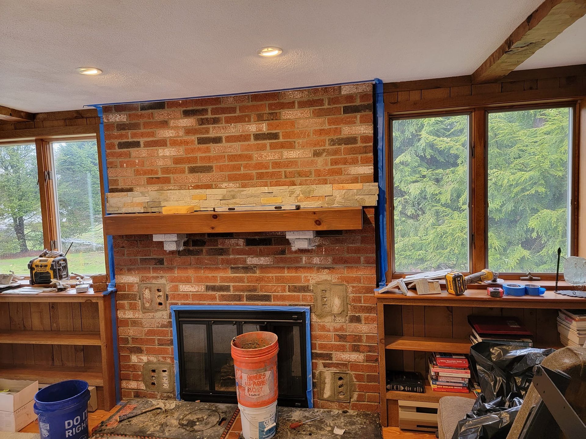 Brick fireplace under renovation with blue tape, fireplace insert, and built-in bookshelves.