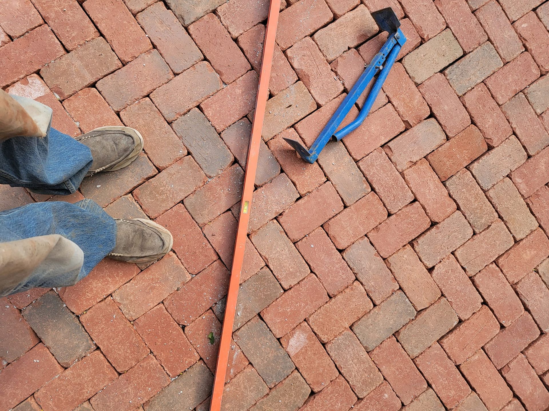 Brick pavement with a person's feet, level, and tool.