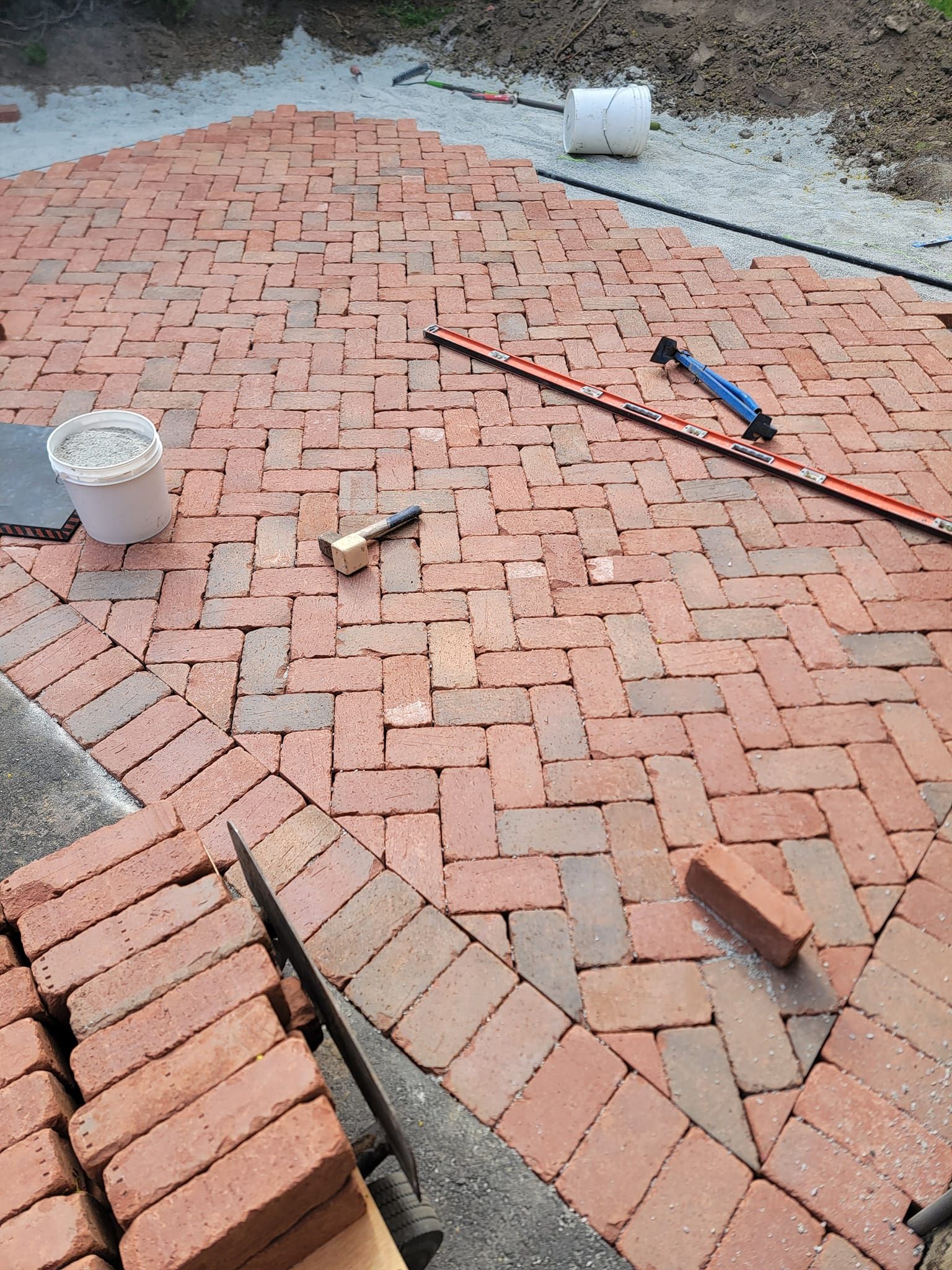Brick patio being constructed with red bricks in a herringbone pattern.